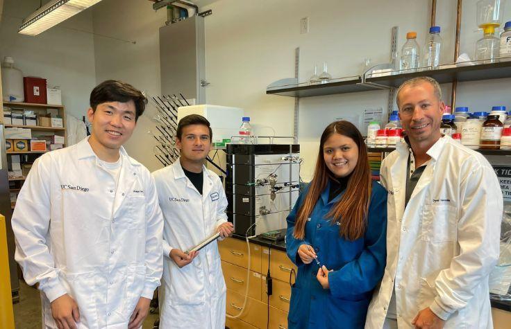 Three students in a lab with a teacher.