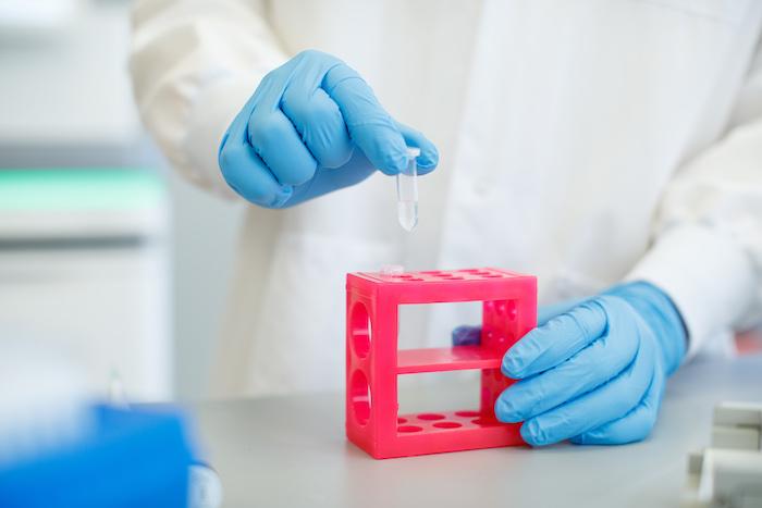 Illumina scientist; gowned and gloved removes a test tube from a rack.