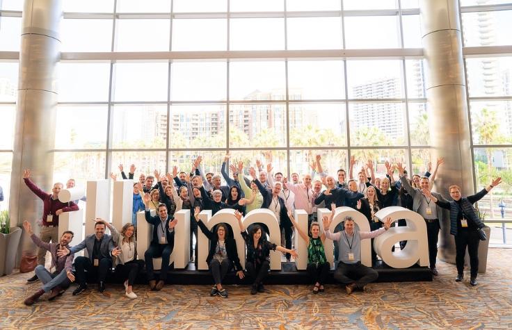 Illumina employees seated in front of the Illumina logo in the corporate headquarters.