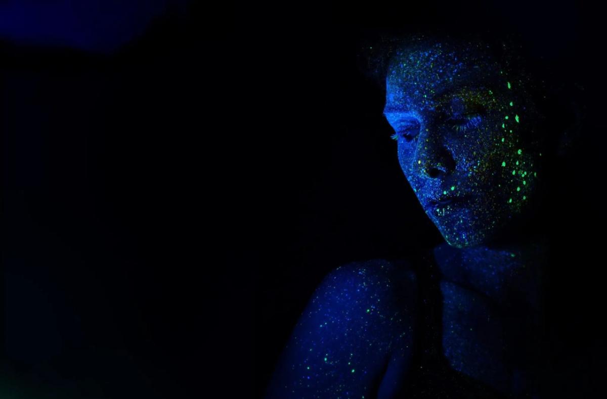 a dark space, a face lit by blue-light on the right, green paint spatters on the face