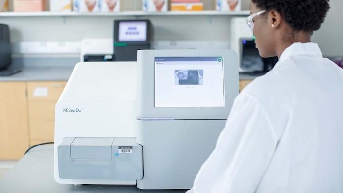 Gowned female Illumina scientist operating a MiSegOx sequencer.