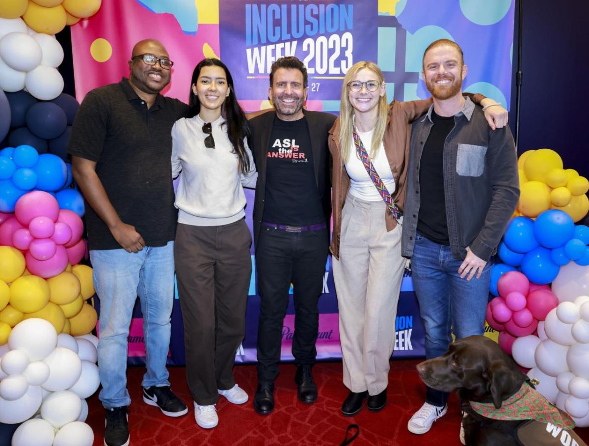 Five people posed with arms around each other. Balloons and "Inclusion Week 2023" behind them.