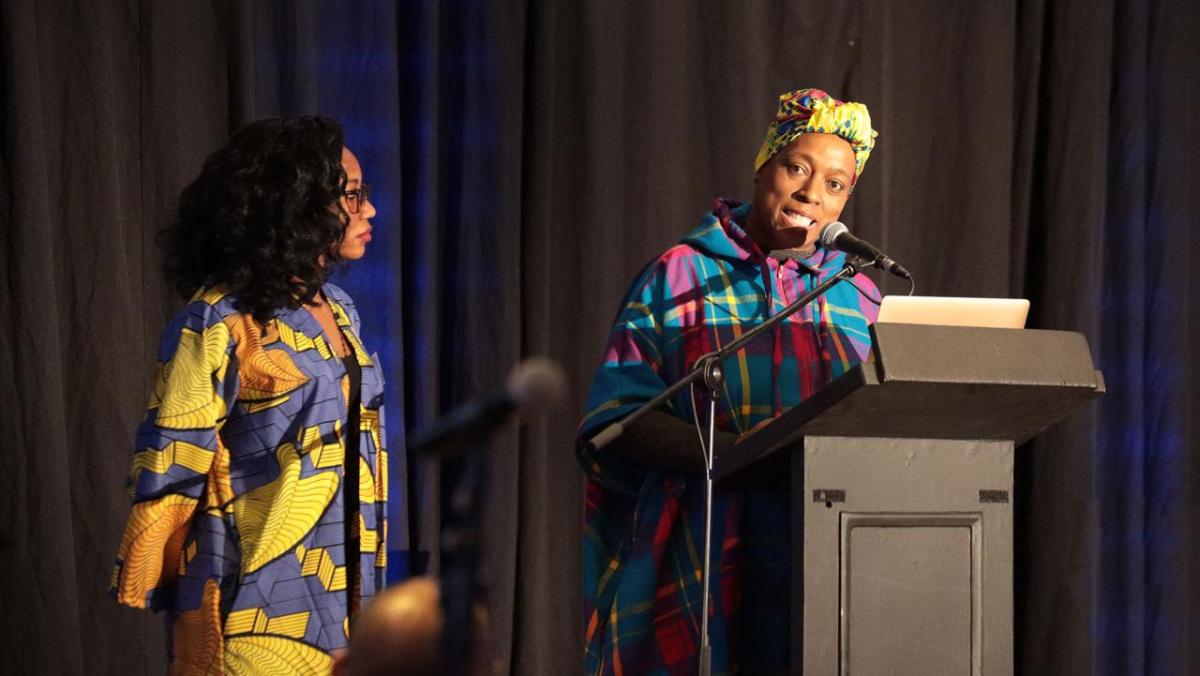 Bridget Ndagaano and Yvette Raphael on stage. Yvette behind a podium with microphone.