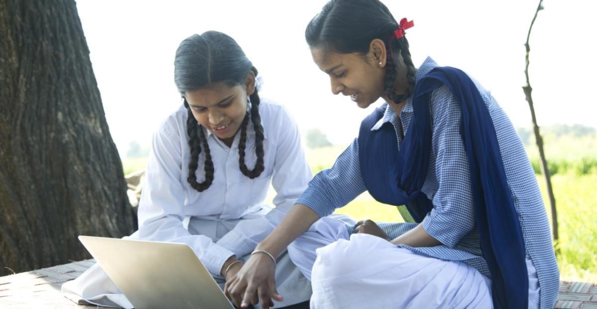 Two children outdoors under a tree looking at a laptop screen