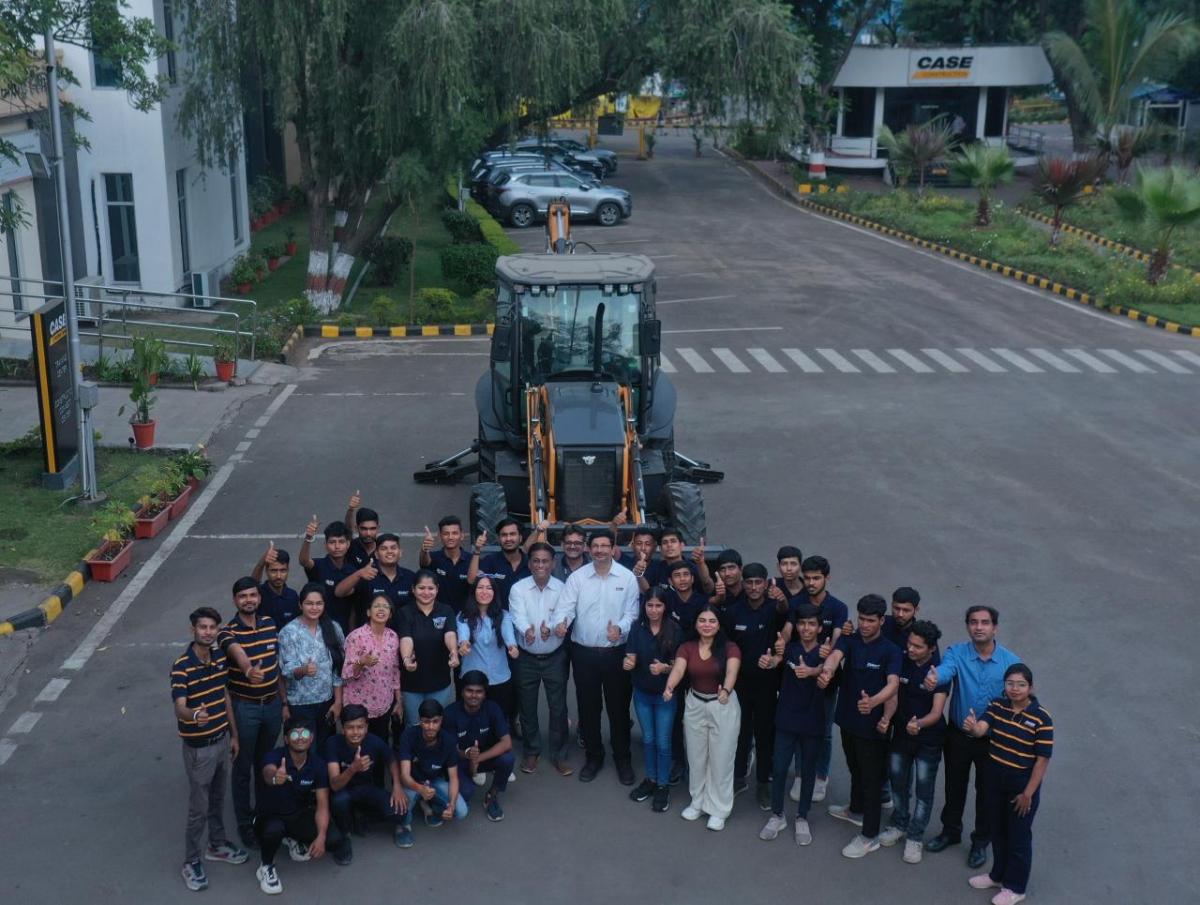 Aerial view of a group of people posed in front of large tractor, each giving 'thumbs-up'.