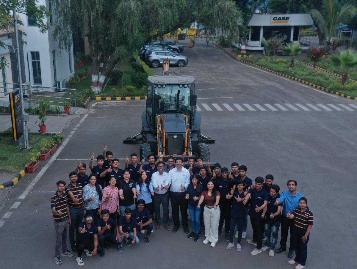 Aerial view of a group of people posed in front of large tractor, each giving 'thumbs-up'.