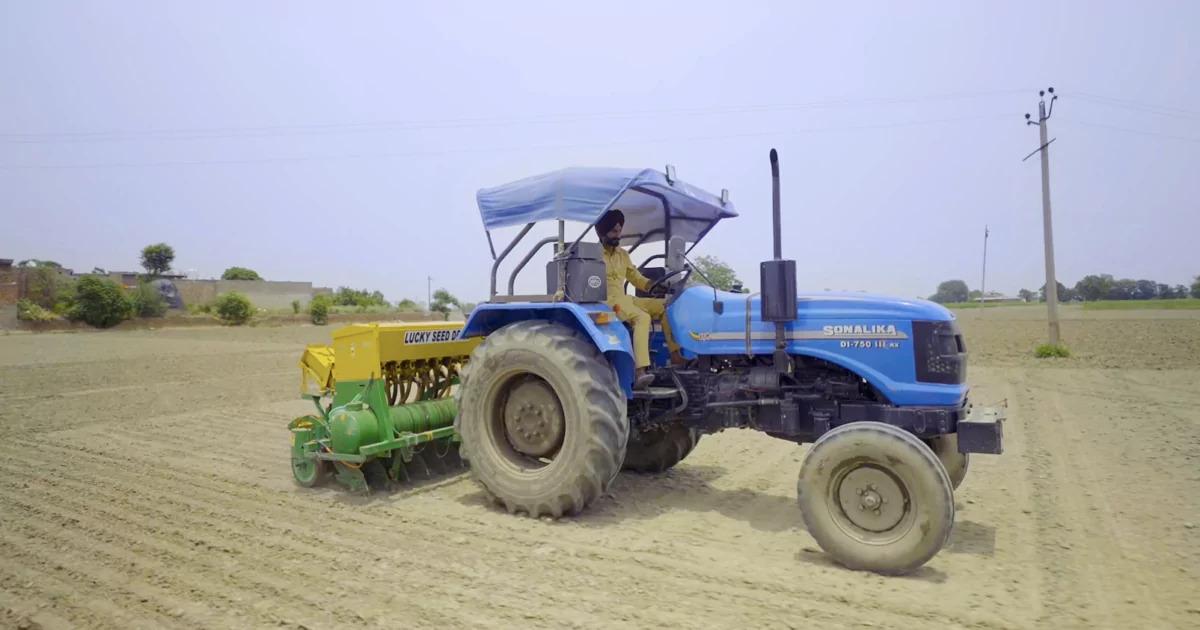 A person in a tractor doing over bare fields.