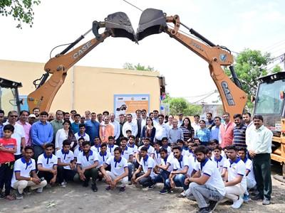 A group of people posed under two tractors with extended bucket arms.