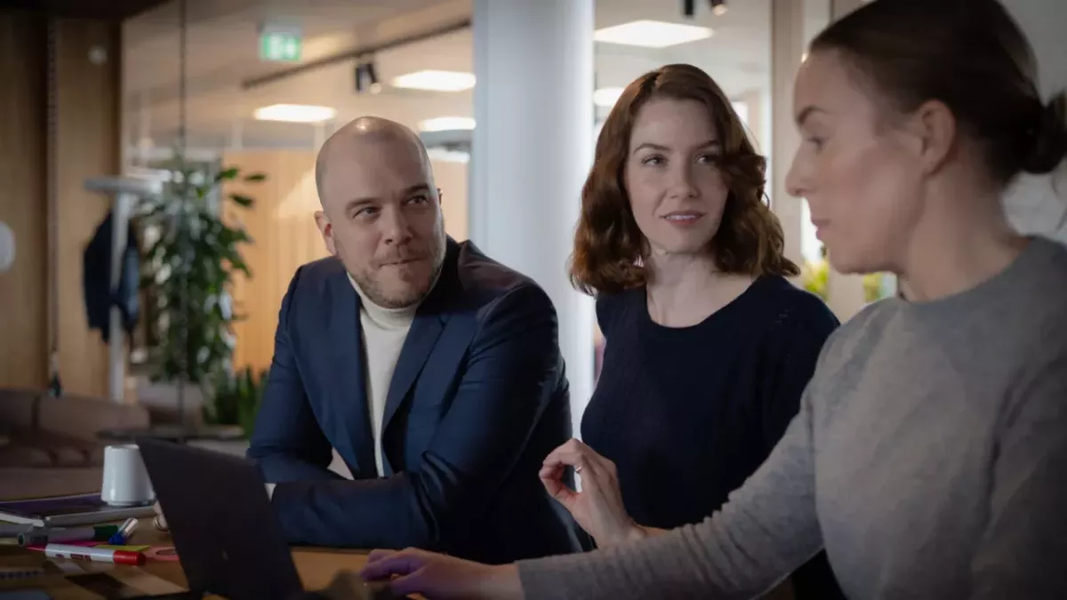 Three people sat at a desk with a laptop 