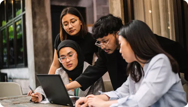 Four people look over a laptop