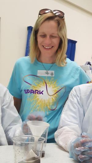 A woman in a blue SPARK™ MilliporeSigma t-shirt engages with students.