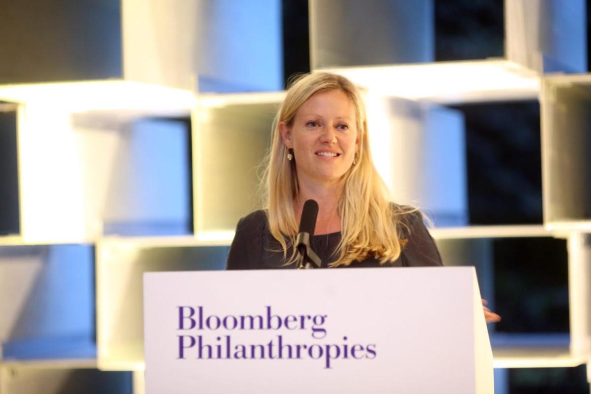 Jemma Read at a podium with a microphone. A wall of lighted cubes behind them. 