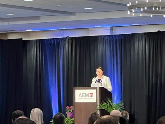 Jill Wiggins, part of CNH’s Global AG Parts & Service’s Service & Maintenance Development team, is the first woman to chair the Conference for AEM in its 33-year history A person stood behind a podium giving a speech