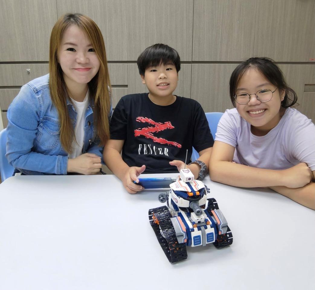 3 people sitting at a table with remote controlled robot