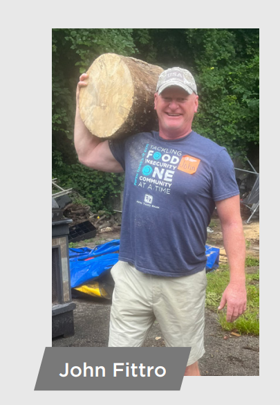 John Fittro holding a large log on one shoulder.