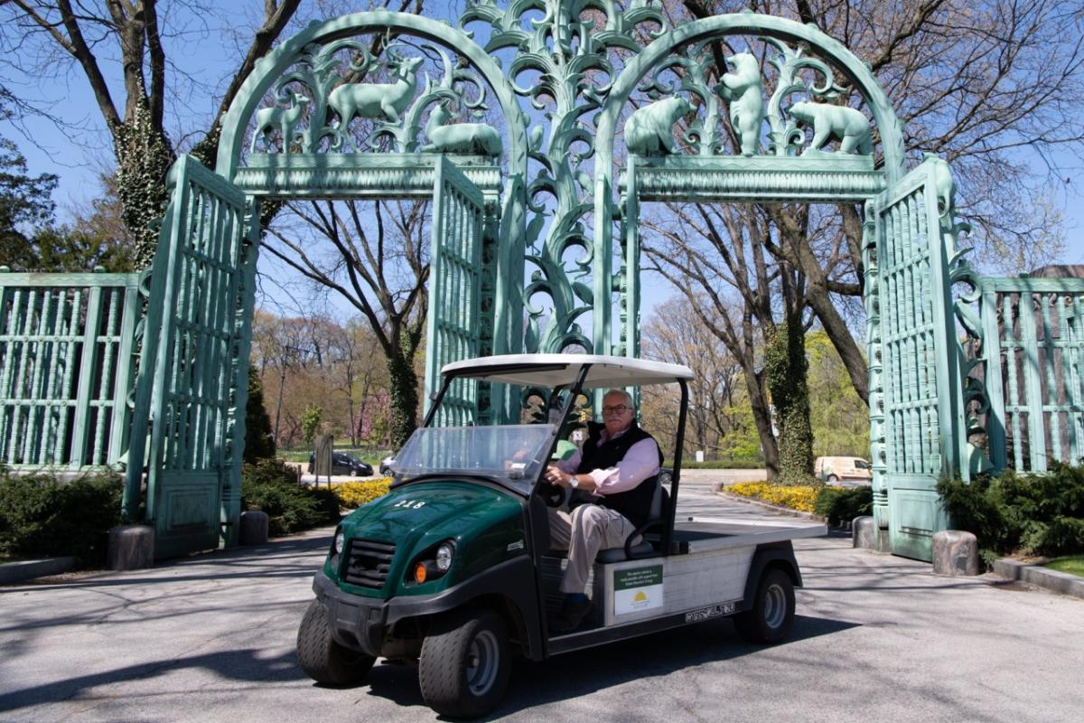 Jim Breheny, director of the Bronx Zoo, sits in one of the new electric vehicles in front of two large gates.