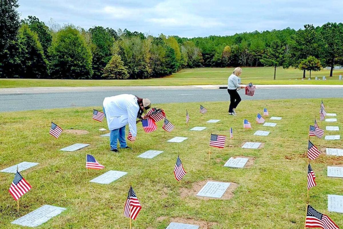 Kay Goke at a cemetery, positioning American flags over graves