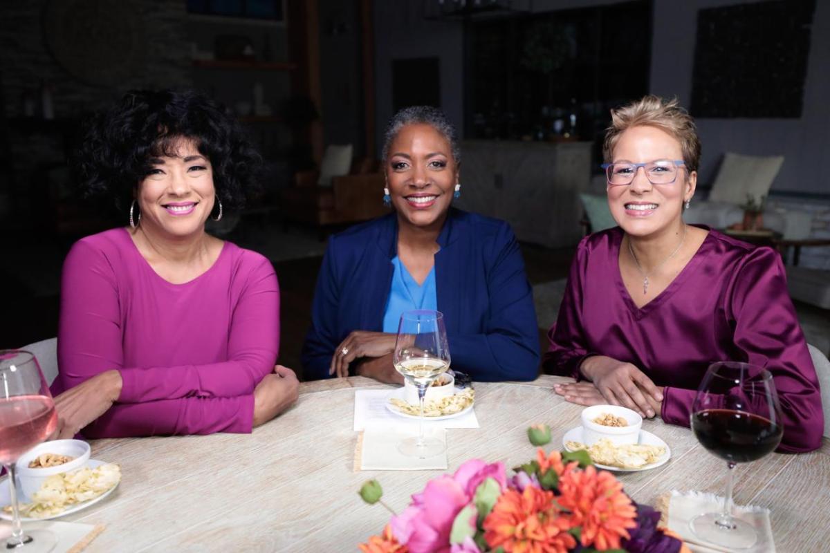QVC Hosts Leah Williams, Jayne Brown and Rachel Boesing are seated at a table  while on-set at QVC Studios.