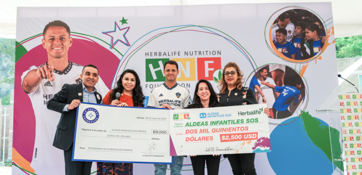 Five people in front of a large banner, holding up two checks.