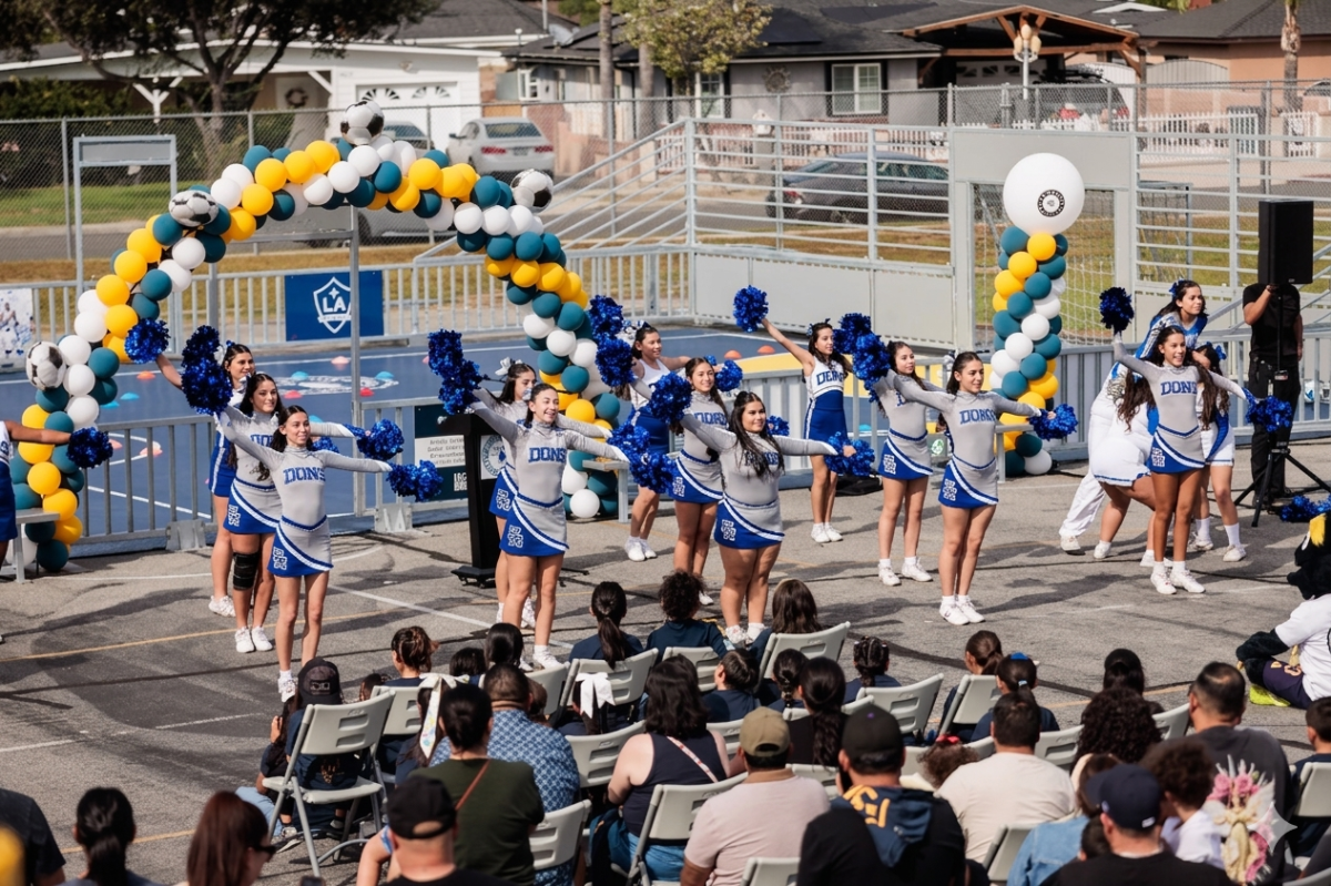 School cheerleaders performing a routine on a blue outdoor soccer court.