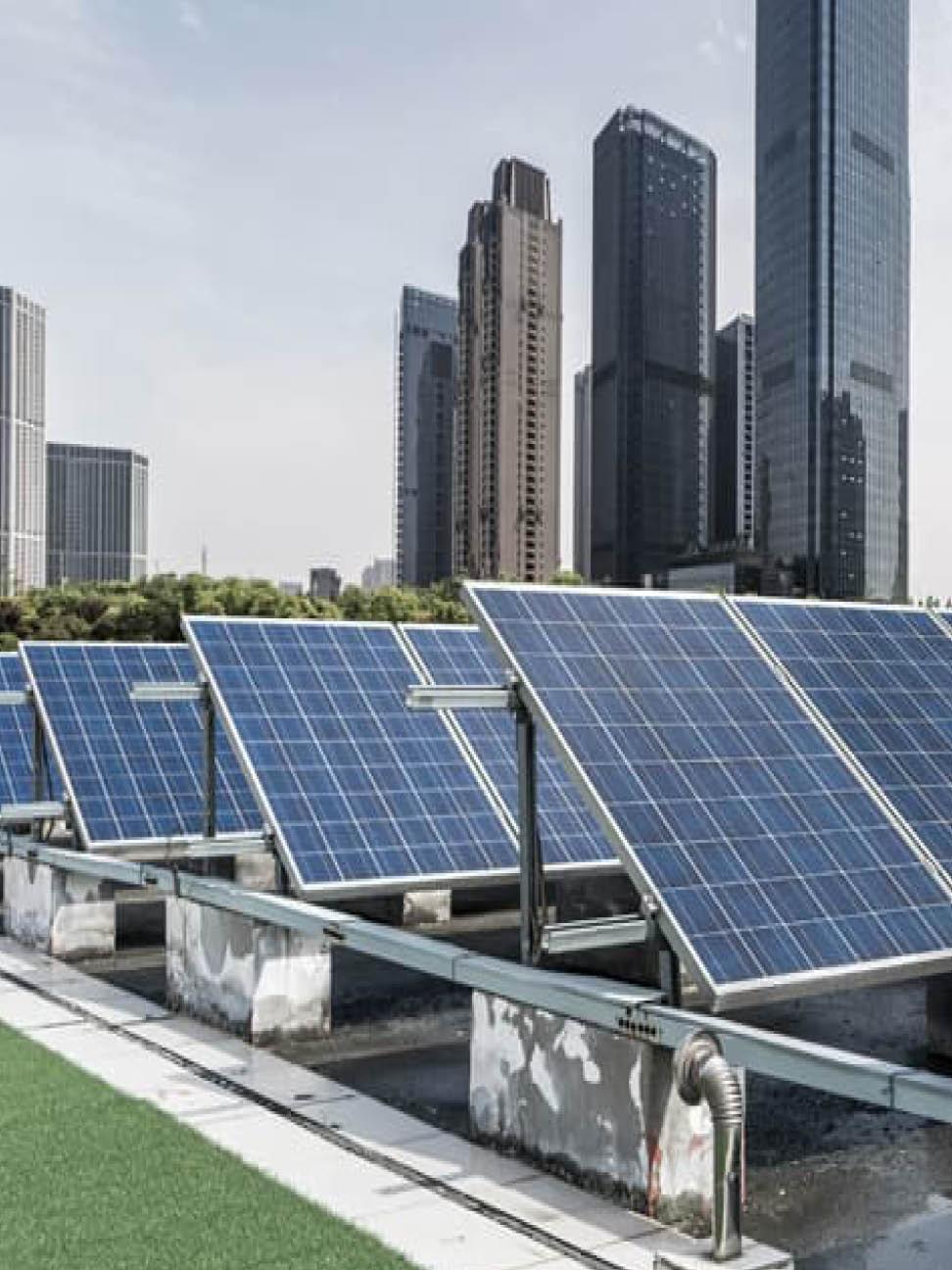 A row of tilted solar panels, a city-scape behind them
