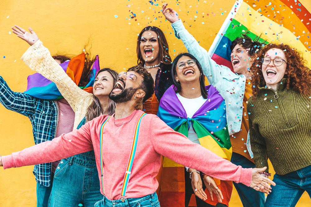 Diverse group of people celebrating together with Pride flags and confetti