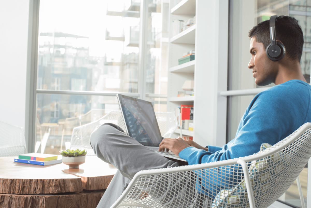 Person wearing headphones, sat on a chair with a laptop on their lap