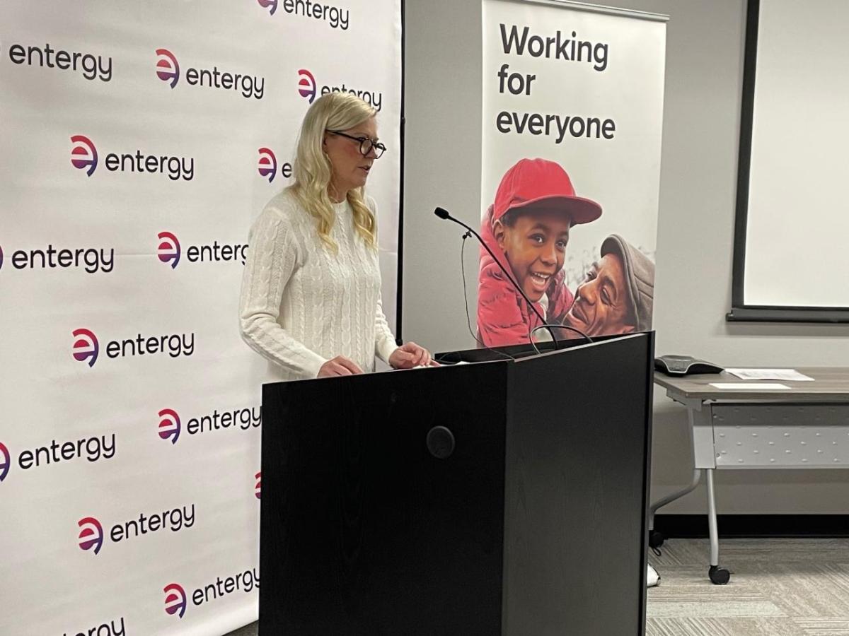 A person stood at a microphone stand, in front of an Entergy backdrop