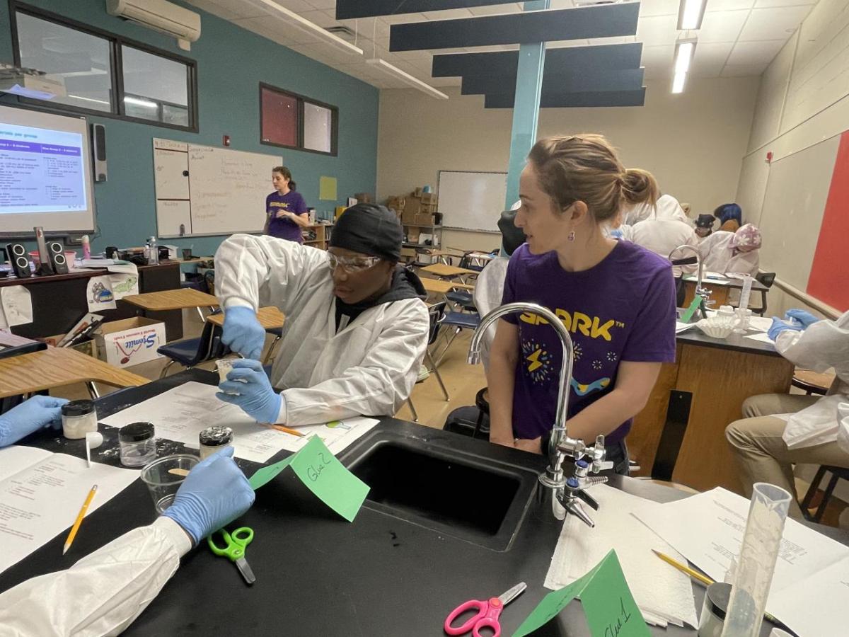 A woman in a purple SPARK™ MilliporeSigma t-shirt engages with students on science lessons. 