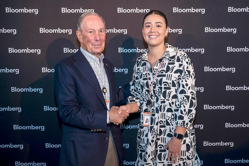 Two people shaking hands for a photo against a Bloomberg backdrop