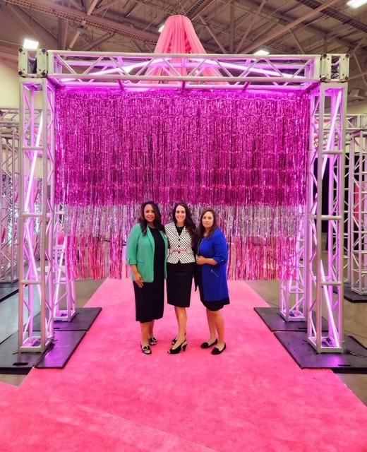 Three people posing for group picture against pink backdrop