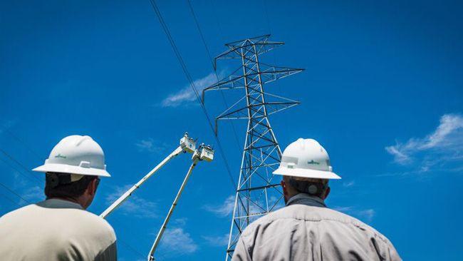 Two lineworkers wearing safety helmets looking up at a transmission tower