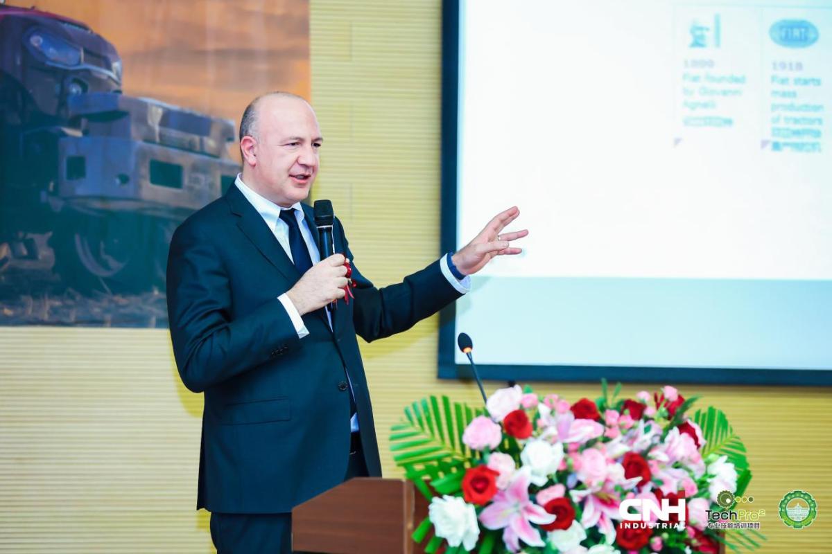 An event speaker holding a microphone while stood next to a projector board 