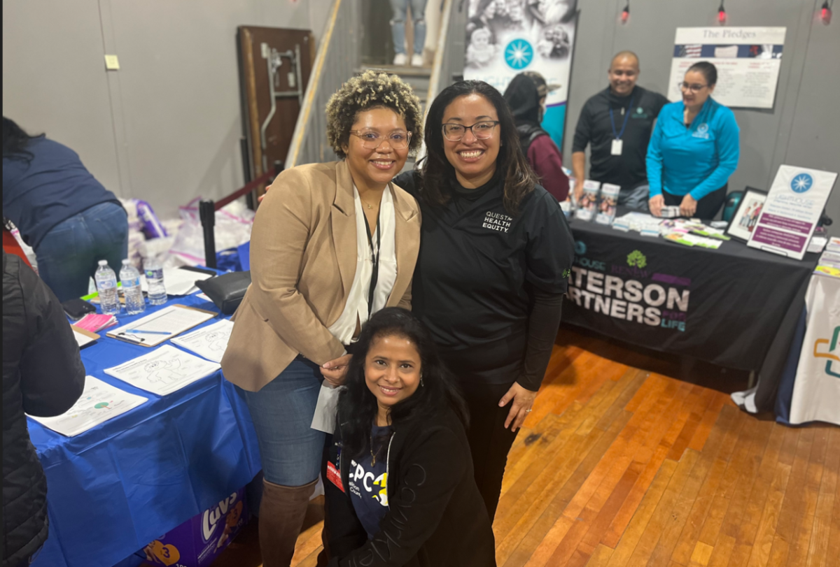 Three people pose for the camera in front of tables set up for different organizations.