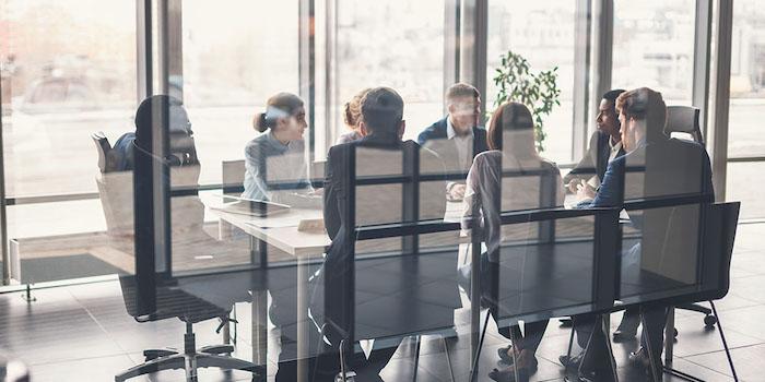 Group of eight men and women of diverse ethnic backgrounds are sitting at a boardroom table.