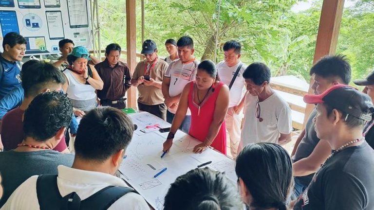 Mabel Celma López Cruz (Yanesha mapping specialist) shared her design ideas with Kichwa, Wampis, and Shipibo peers at a Mapeo workshop Chazuta, San Martin, Peru organized by Forests Peoples Program. (November 2023) Mabel pointing a a map surrounded by others.