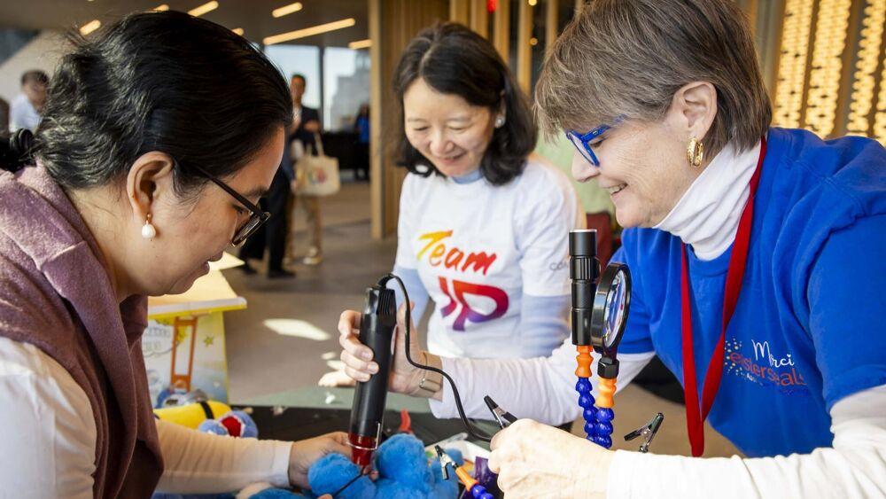 Three people stood around a table helping to modify toys for children with disabilities 