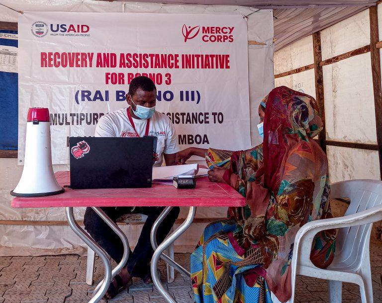 Meshach Malagwi  pictured here registering a community member for monthly e-vouchers so she can purchase food for her family.