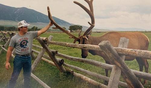 Mike Maloney touching the antlers of a large elk behind a fence.
