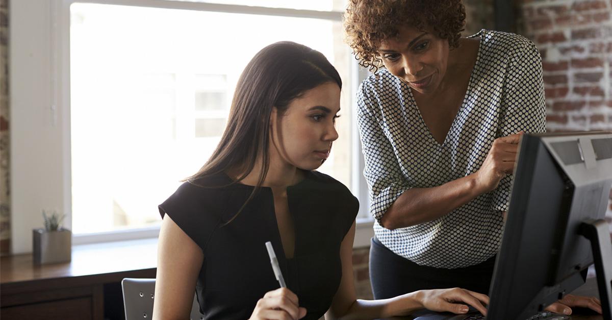 Older woman stands behind young woman on the computer