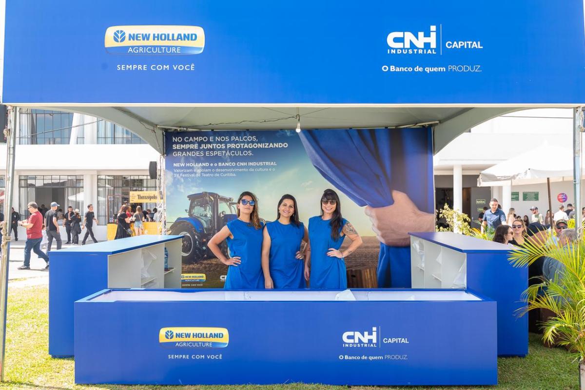 Three people in blue shirts at an outdoor covered booth with signs in blue for New Holland and CNH
