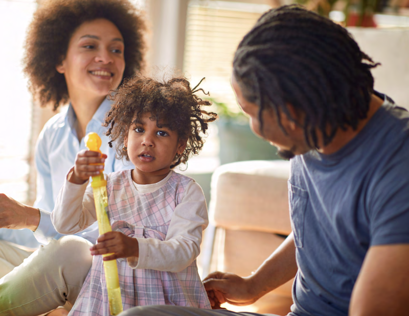 A family seated with their daughter holding a toy.