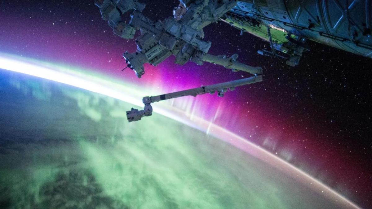A large piece of equipment in outer space. The Earth in the background lit up in green and purple lights.
