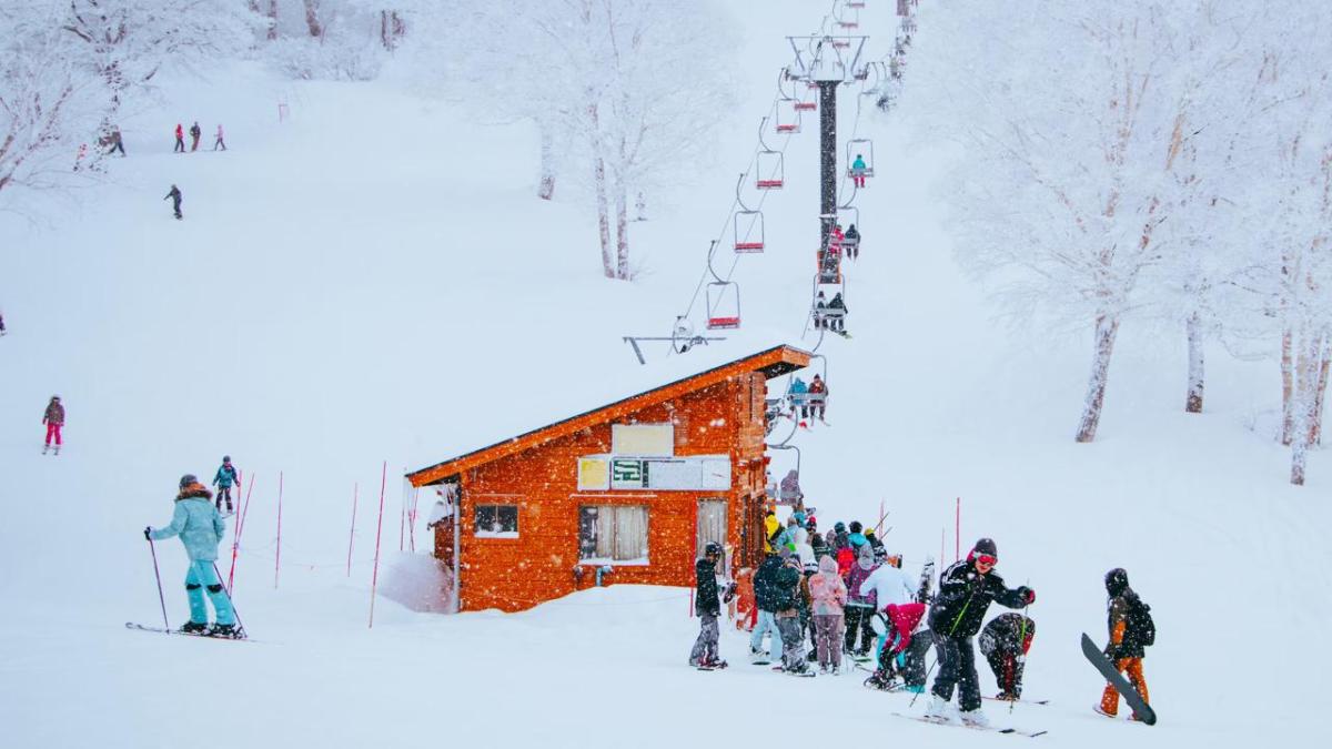 A group of skiers at the bottom of a ski lift and hill on a snowy day.