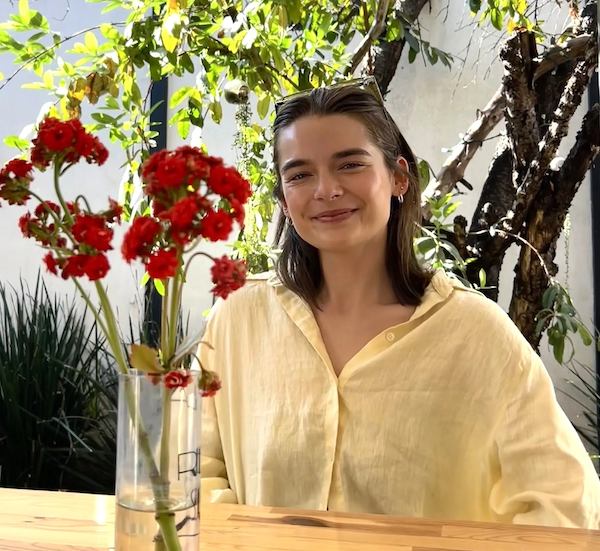 Natalie seated at a table with a vase of red flowers on the table.