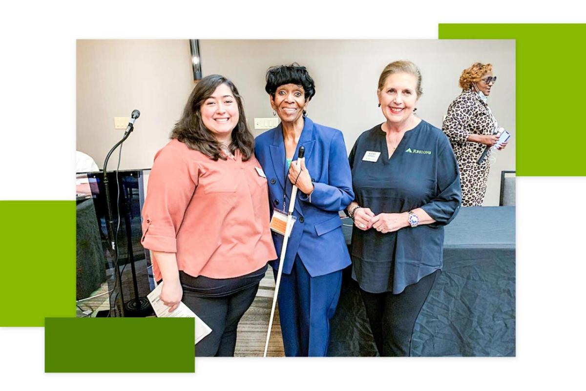 A woman in a blue suit holding a white mobility cane surrounded by 2 bank representatives