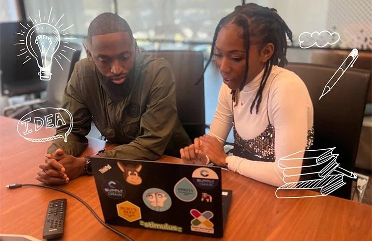 Two people sat next to each other at a table, looking at a laptop