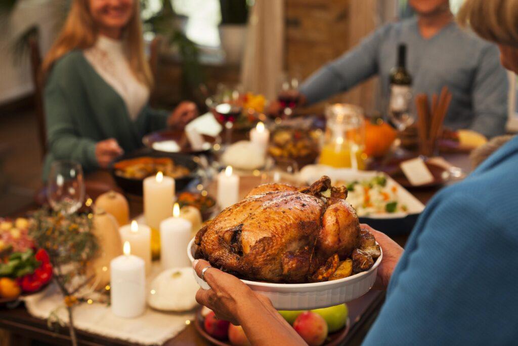 Thanksgiving dinner table with guests and a turkey are shown.