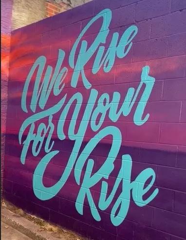 sign reading, "We Rise For Your Rise"