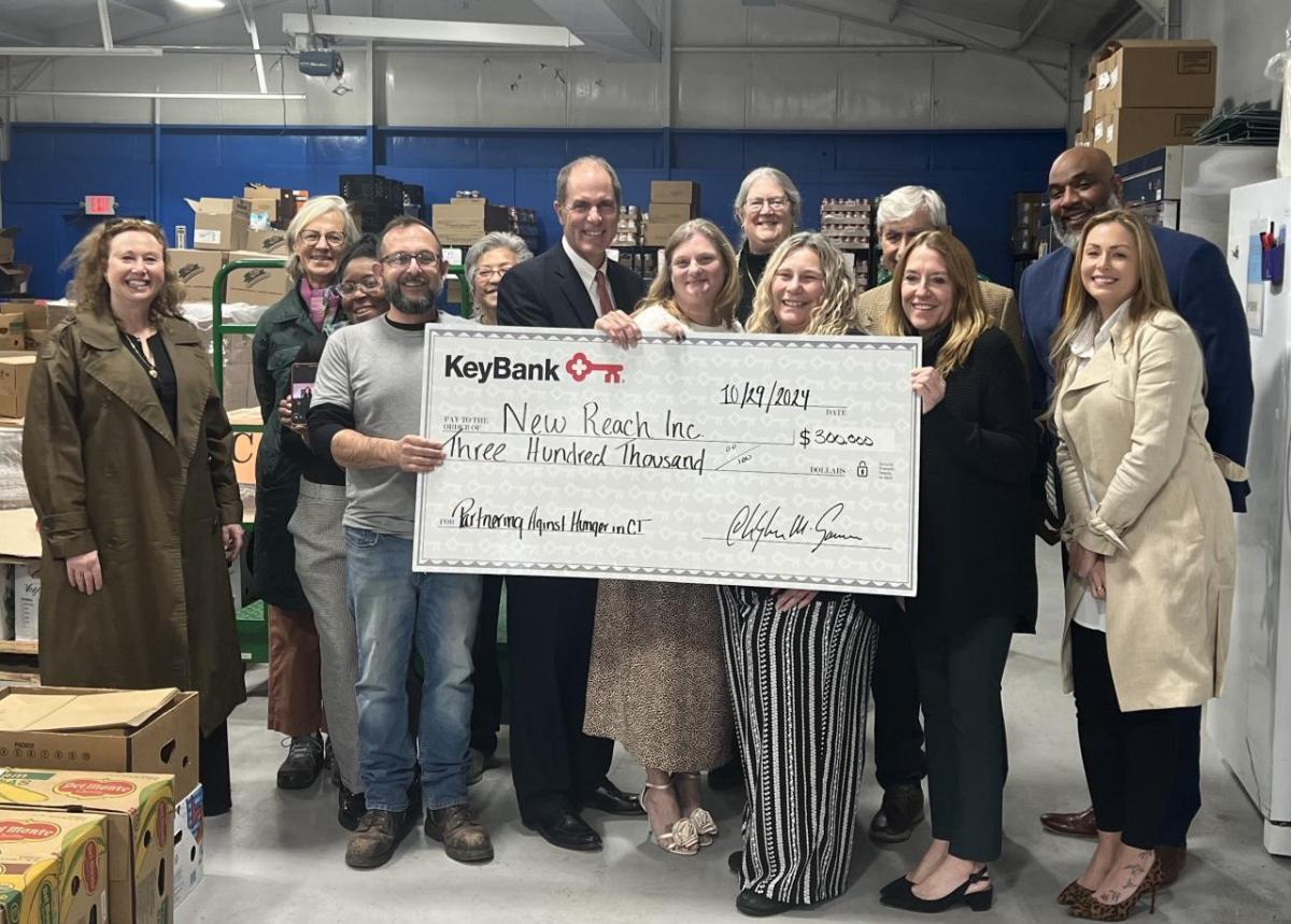 Leaders from KeyBank, New Reach/FISH and board members gathered at FISH’s Warehouse on Peck Street in New Haven for a check presentation. Pictured from left: Jane Glassman, New Reach Board Member; Julia Hunt Bogardus, New Reach Board Member; Chelsea Reid, New Reach Director of Operations; Joe Arnone, FISH Operations Manager; Nancy Williams, FISH Pantry Manager; Matt Hummel, KeyBank Market President; Jocelyn Antunes, New Reach Program Director; Kristin Bures, KeyBank Business Banker; Meredith Clay, New Reach Chief Quality and Compliance Officer; William Dow, New Reach Board Member; Tara Courtmanche, New Reach Board Member; Dwayne Hicks, KeyBank Branch Manager; and Analisha Michanczyk, KeyBank Corporate Responsibility Officer. New Reach and KeyBank team shown with grant check.